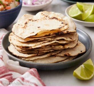 Pinterest graphic of a stack of corn tortillas on a plate with limes, onions, salsa, and jalapeno in the background.