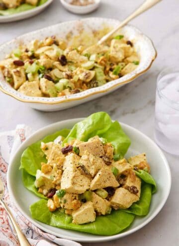 A plate of curried chicken salad over lettuce with a platter of more chicken salad in the background.