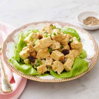 A plate of curried chicken salad over lettuce with a fork and bowl of pepper off to the side.