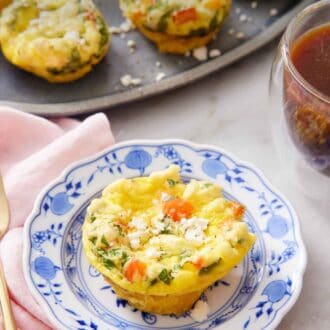 Pinterest graphic of a plate with an egg muffin topped with crumbled feta cheese. A platter with more egg muffins and a coffee behind the plate.