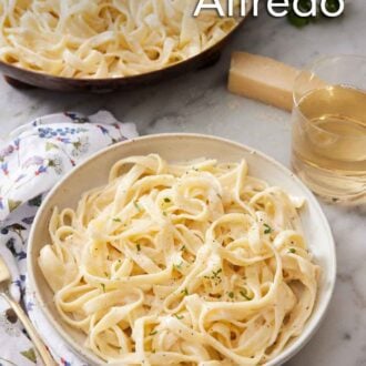 Pinterest graphic of a bowl of fettucine alfredo with a glass of wine and a skillet with more pasta in the back.