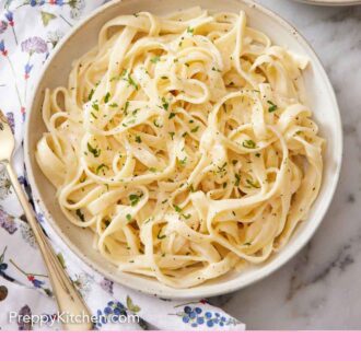 Pinterest graphic of an overhead view of a plate of fettucine alfredo with chopped parsley on top. A fork on a linen napkin beside it.