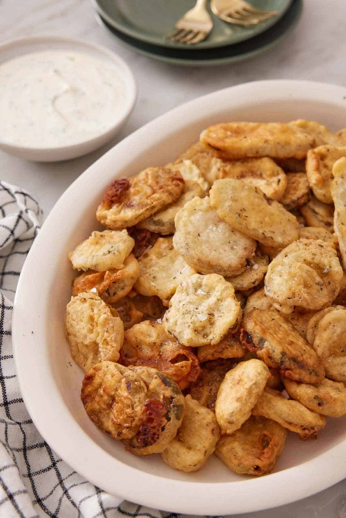 A platter of fried pickles with a bowl of sauce in the background.