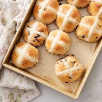Overhead view of a baking dish of hot cross buns with a couple taken out.