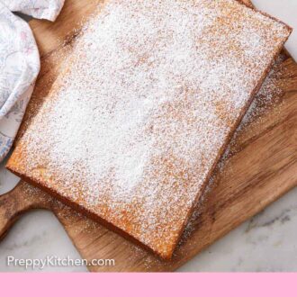 Pinterest graphic of an uncut slab of hot milk cake dusted with powdered sugar on a wooden serving board.