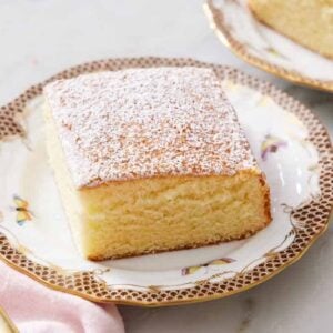 A plate with a slice of hot milk cake topped with powdered sugar with a fork beside it.