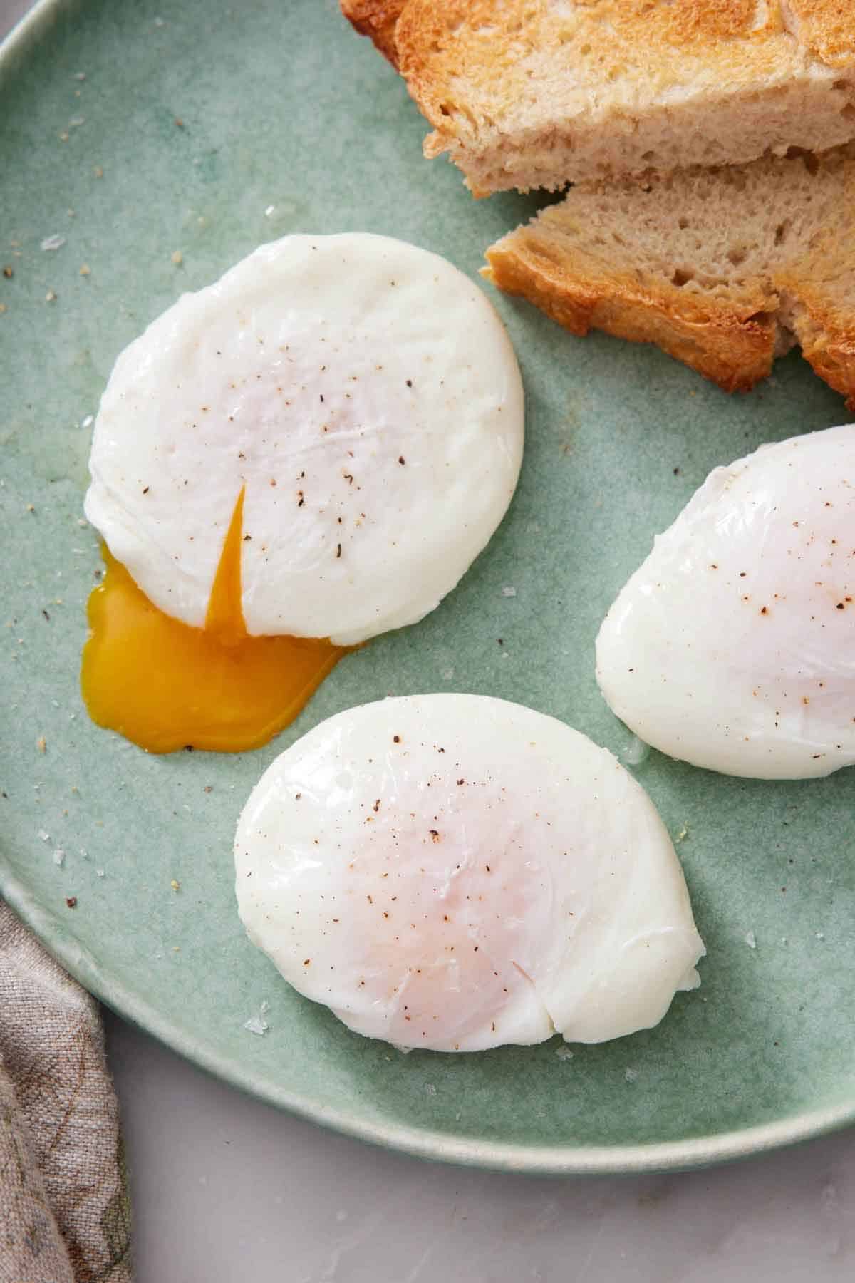 A plate with three poached eggs, one slightly cut with the yolk oozing out.