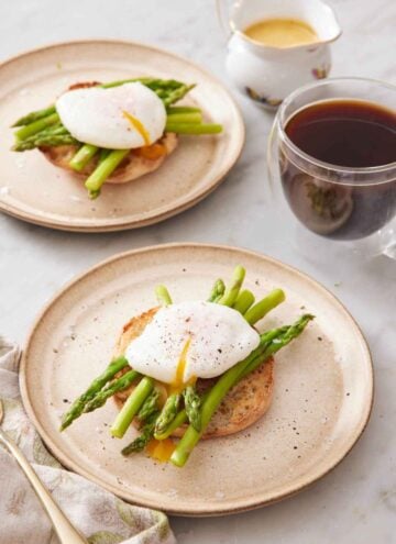Two plates with a bagel topped with asparagus and a poached egg. A coffee and sauce off to the side.