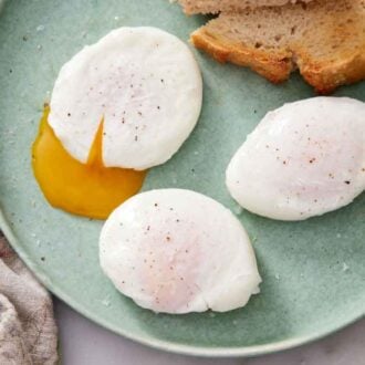 A plate with three poached eggs by toasted bread, one egg slightly cut with the yolk oozing out.