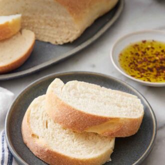 Pinterest graphic of two slices of Italian bread on a plate with the rest of the cut loaf in the background along with a plate of seasoned oil.