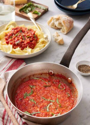 A pot of marinara sauce with torn bread in the back and a bowl of noodles with marinara sauce on top.