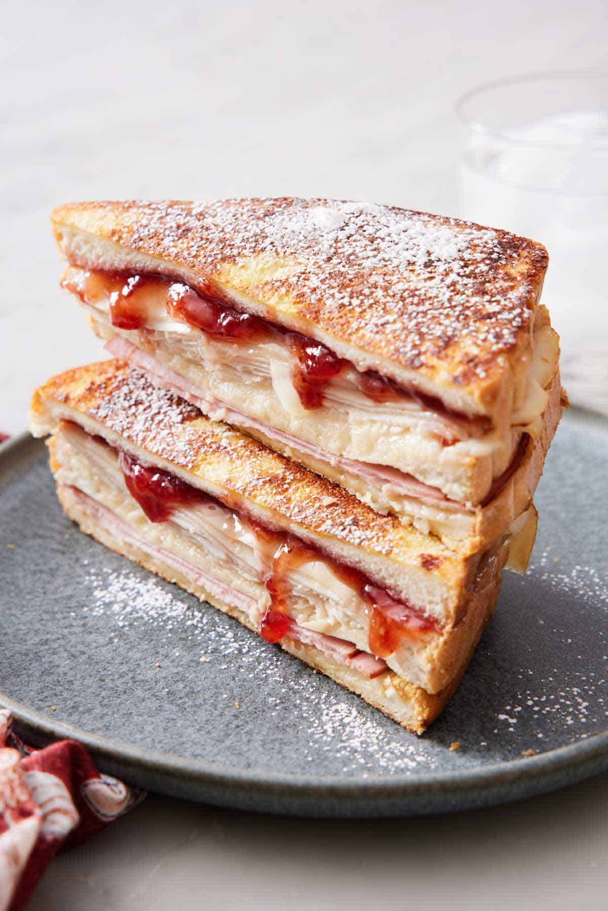 A plate with two halves of a Monte Cristo sandwich stacked on top of each other and dusted in powdered sugar.