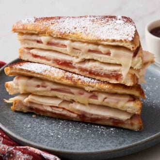 A stack of two halved Monte Cristo sandwich on a plate topped with powdered sugar.