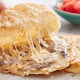 A hand lifting up the top tortilla of a mulita showing the melty cheese.