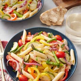 Pinterest graphic of a bowl of pasta primavera with a second bowl in the background and bread torn on the side with a glass of wine.