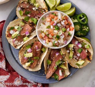 Pinterest graphic of an overhead view of a platter of steak tacos along with a bowl of salsa, lime wedges, and jalapenos.