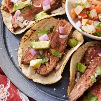 Overhead view of steak tacos on a platter with a bowl of salsa.