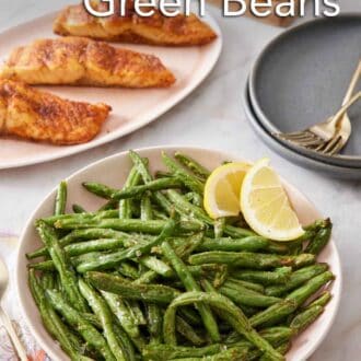 Pinterest graphic of a plate of air fryer green beans with lemon wedges. Platter of salmon in the back along with cut lemons and plates and forks.