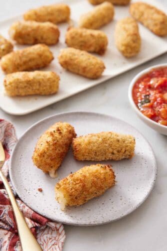A plate with three air fryer mozzarella sticks with a platter in the background with more.