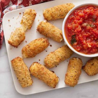A platter of air fryer mozzarella sticks with marinara sauce. One torn with the cheese pulled.