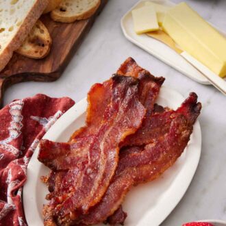 Pinterest graphic of a plate of candied bacon with butter, bread, berries, and eggs around it.
