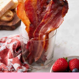 Pinterest graphic of a glass cup of candied bacon. A platter in the background with fried eggs and sliced bread.