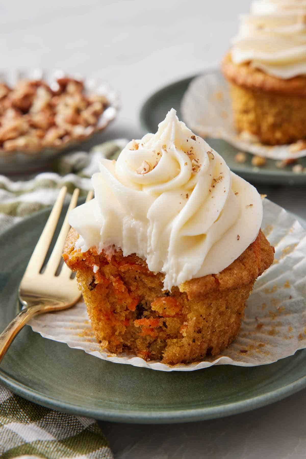 A carrot cake cupcake on a plate with the liner pulled down and a bite taken out of it.