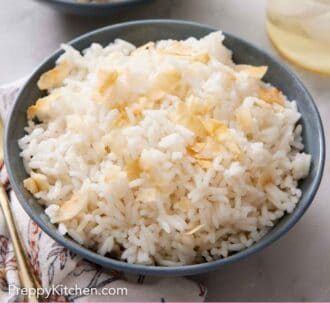 Pinterest graphic of a bowl of coconut rice topped with toasted coconut. A glass in the back along with another bowl of rice.
