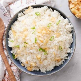 Overhead view of a bowl of coconut rice with green onions and toasted coconut as garnish. A bowl of coconut and a spoon on the side.