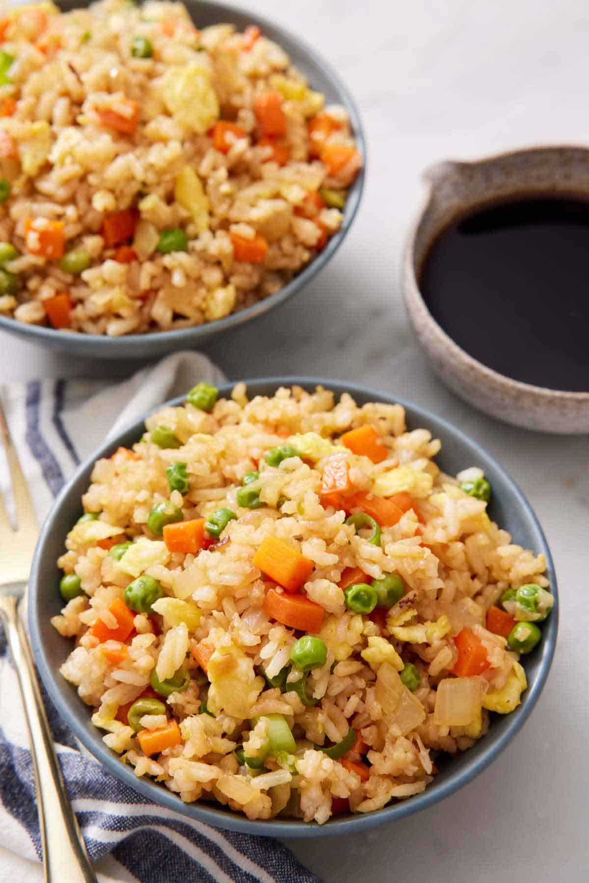 Two bowls of fried rice with a bowl of sauce off to the side.