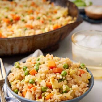 Pinterest graphic of a bowl of fried rice with a skillet of more in the background along with a drink.