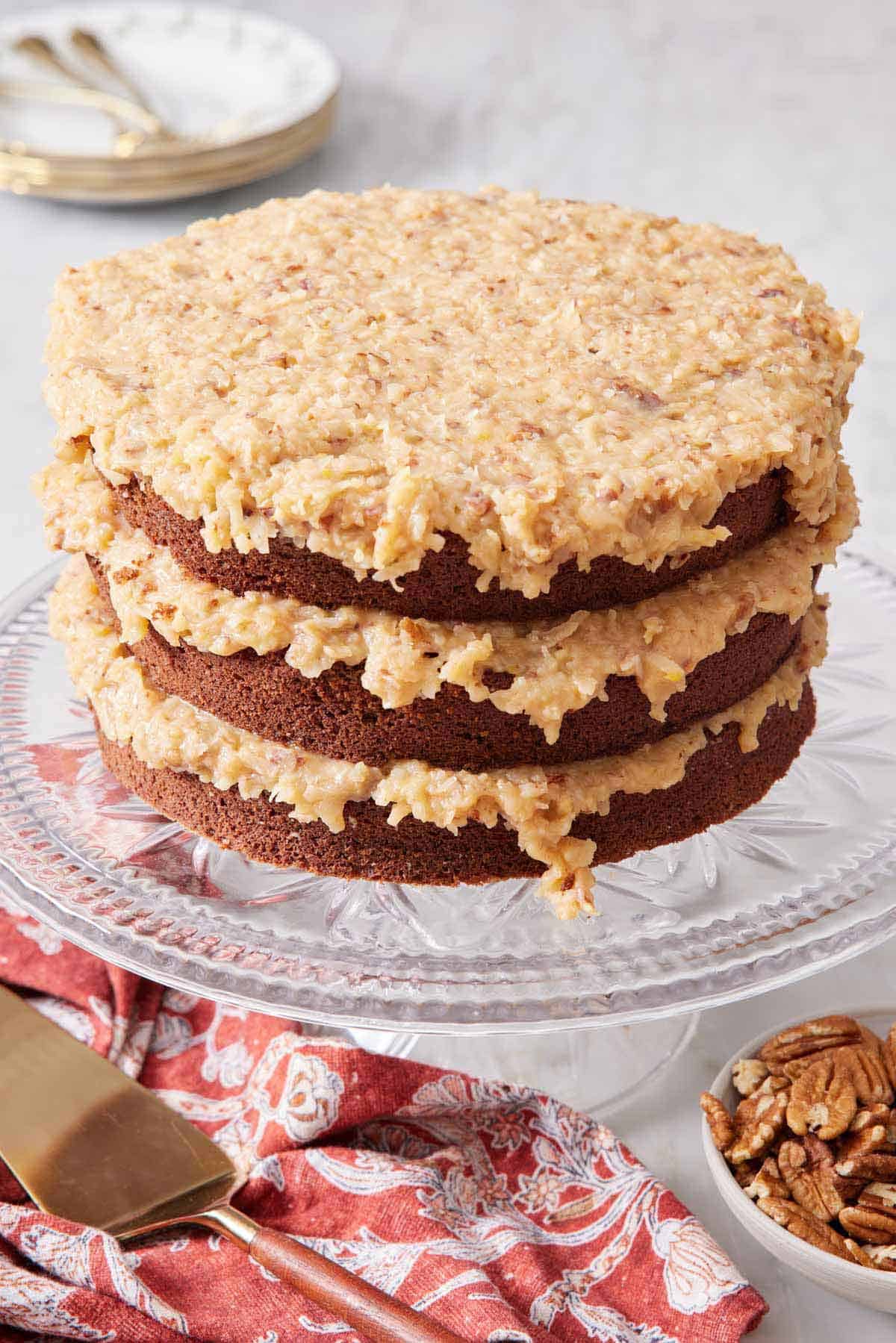 A cake stand with a German chocolate cake with three cake layers with frosting in between each layer.