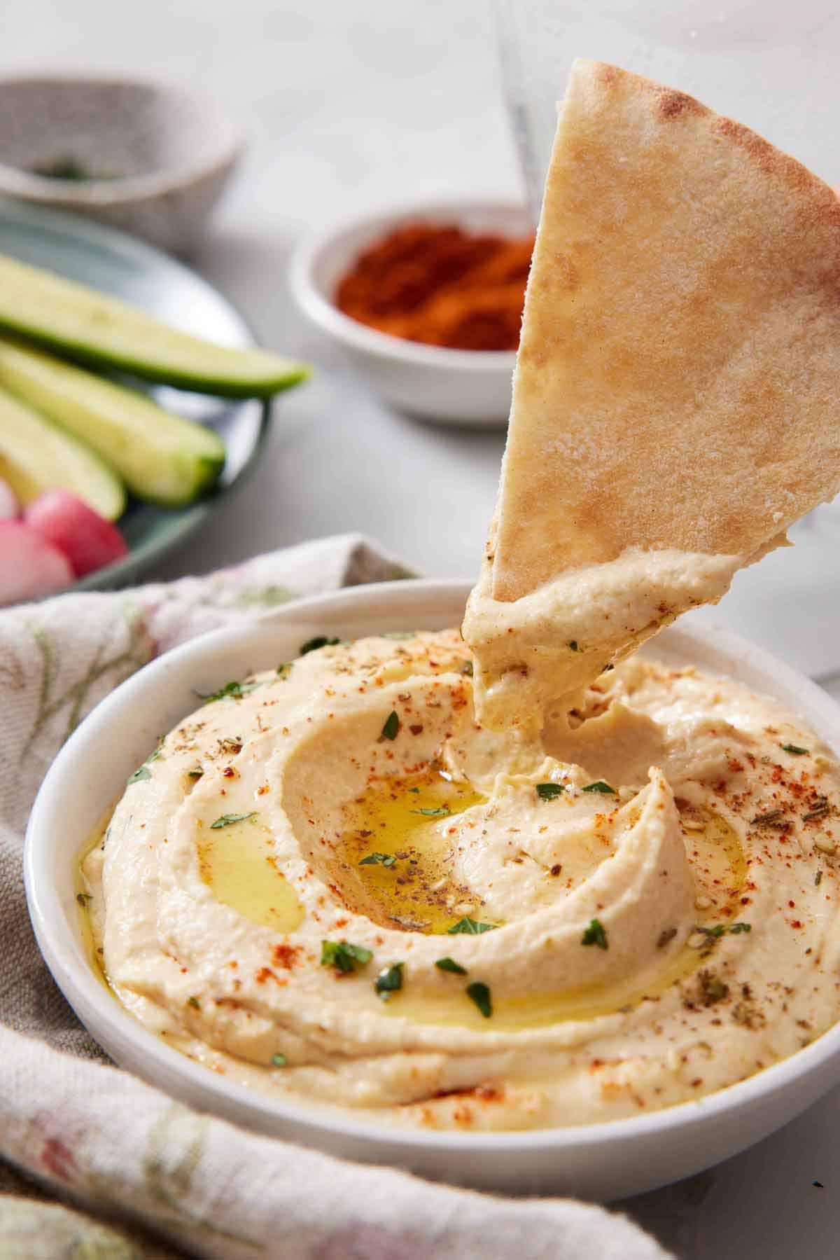 A piece of pita bread dipped into a bowl of hummus.