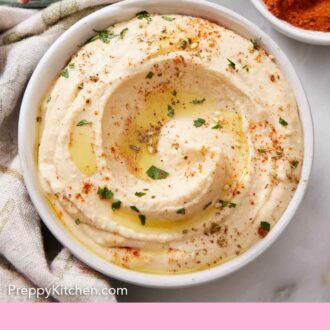 Pintrest graphic of an overhead view of a bowl of hummus with oil, parsley, and paprika as garnish. A bowl of paprika and some radishes in the back.