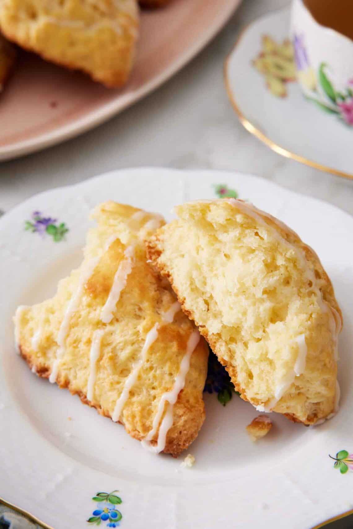 A plate with a lemon scone torn in half. A drizzle of icing over the torn scone.