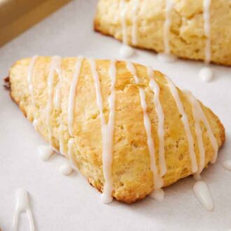 A close up view of lemon scones with icing drizzled on top on a lined sheet pan.