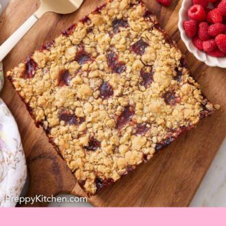 Pinterest graphic of a slab of uncut raspberry bars on a wooden serving board with fresh raspberries on the side.