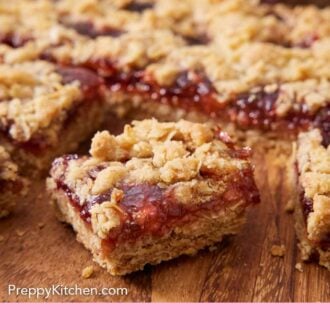 Pinterest graphic of a piece of raspberry bars pulled forward from the rest of the dessert on a wooden board.
