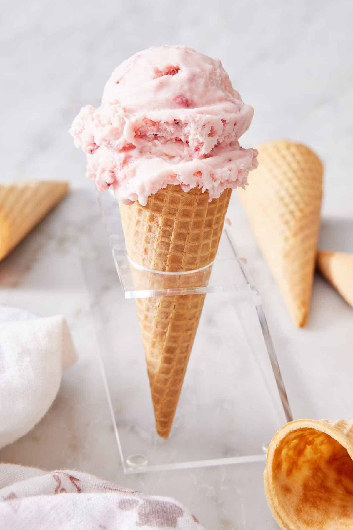 An ice cream cone with two scoops of strawberry ice cream. More cones scattered around.