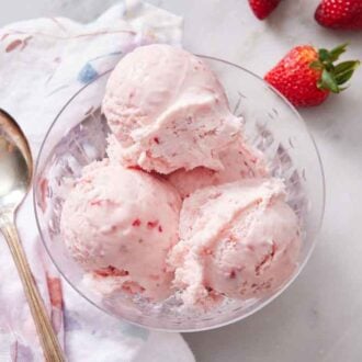 An overhead view of a bowl of strawberry ice cream with a spoon and strawberries beside it.