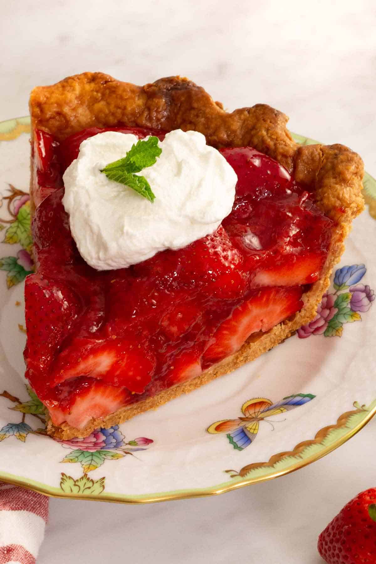 A slice of strawberry pie with whipped cream on top with fresh mint leaves as garnish.