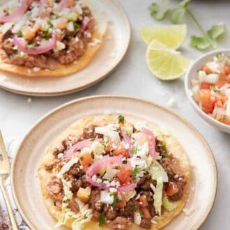Pinterest graphic of a plate with a tostada with a second plate in the background along with cut limes, cilantro, and a bowl of pico de gallo.