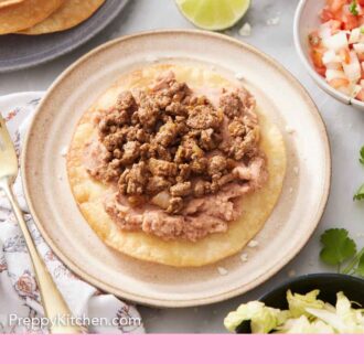 Pinterest graphic of a plate with a tostada with no toppings. A plate of fried tortillas, bowl of pico de gallo, lime wedges, and cooked beef in the background.