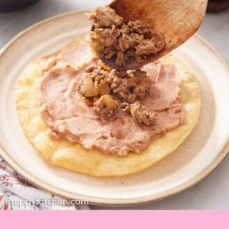 Pinterest graphic of beef spooned onto a plate with a fried tortilla with refried beans to make a tostada.