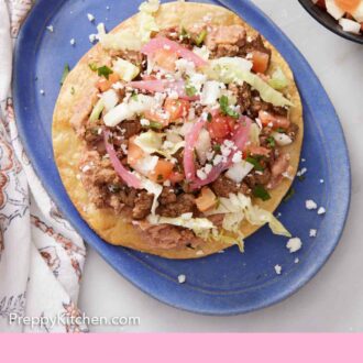 Pinterest graphic of an overhead view of a tostada with various toppings on a blue oval plate.