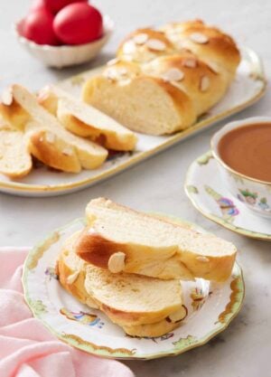 A plate with two slices of tsoureki with a coffee in the back along with a platter with the rest of the bread.