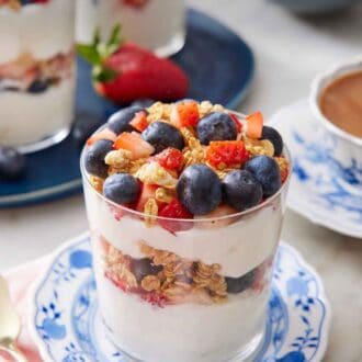 Pinterest graphic of a glass of yogurt parfait on a plate with a platter in the background with two more parfaits.