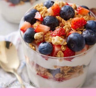 Pinterest graphic of a glass of yogurt parfait topped with chopped strawberries, granola, and blueberries.