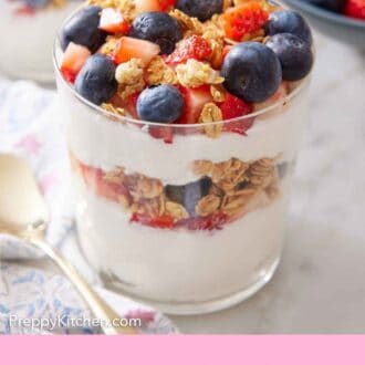 Pinterest graphic of a yogurt parfait with granola, blueberries, and strawberries on top. A spoon beside it.
