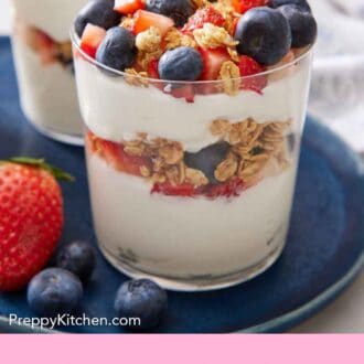 Pinterest graphic of a blue platter with two yogurt parfaits with granola, blueberries, and strawberries.